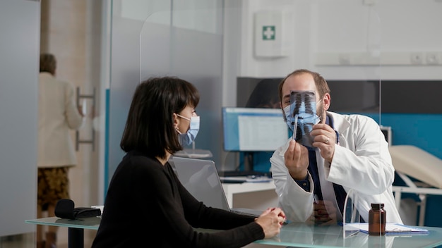 Médecin généraliste expliquant la radiographie osseuse à une patiente lors d'un examen médical. Médecin montrant les résultats des rayons X pour trouver un diagnostic de soins de santé, visite de contrôle annuelle.