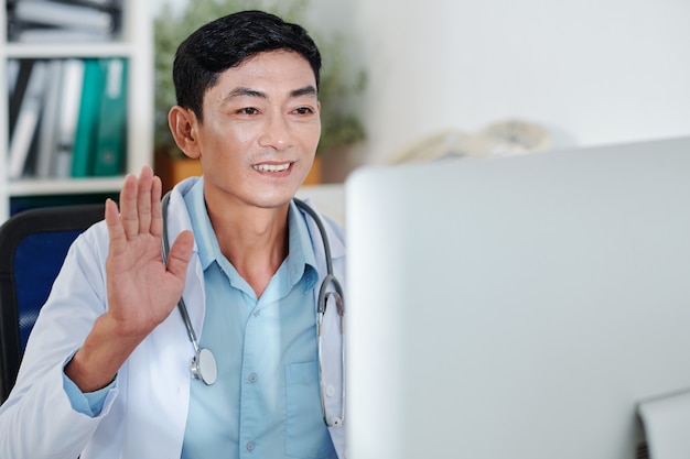 Médecin généraliste mature souriant en agitant la main lors de l'accueil de collègues lors d'une conférence en ligne
