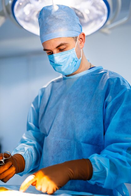 Un médecin en gommage et un masque facial opèrent dans une clinique moderne. Jeune médecin professionnel sur fond de salle de chirurgie. Fermer.