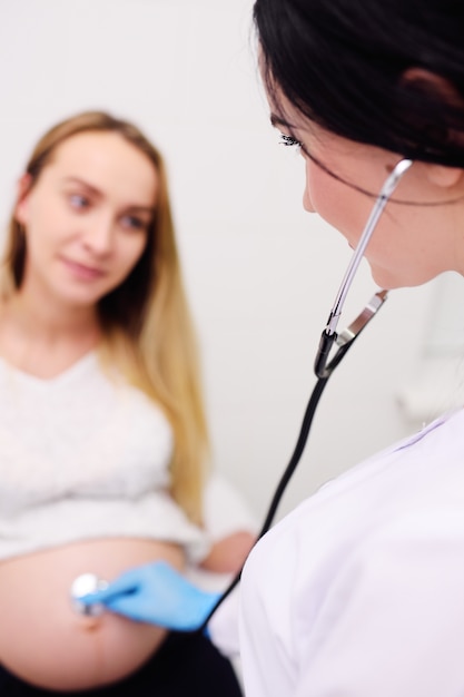 Un médecin gynécologue examine une femme enceinte avec un gros ventre contre une clinique moderne