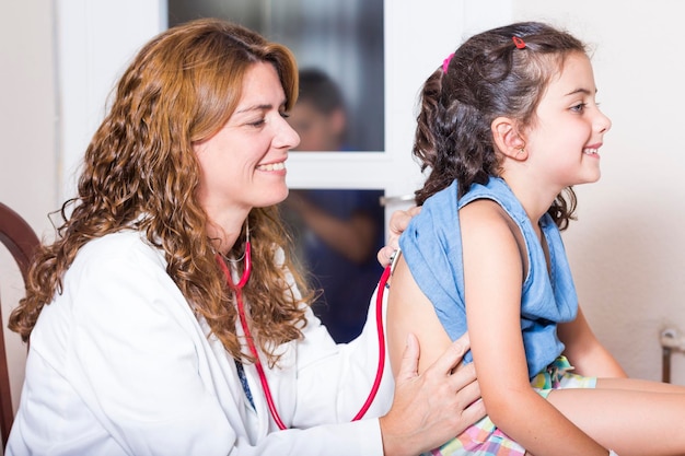 Une médecin heureuse examinant le dos d'une fille dans une salle d'hôpital.