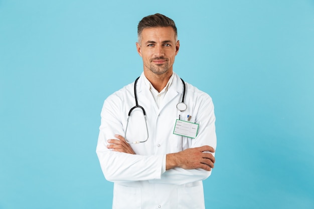 Médecin homme confiant en uniforme debout isolé sur mur bleu, les bras croisés