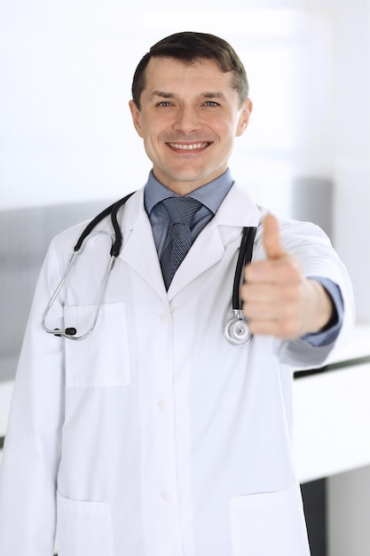 Médecin homme joyeux souriant à la caméra, pouces vers le haut. Service médical parfait en clinique. Heureux avenir dans la médecine et les soins de santé.