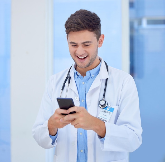 Médecin homme et téléphone avec sourire pour envoyer des SMS ou discuter et bonne connexion à l'hôpital Heureux homme de soins de santé ou professionnel de la santé souriant pour le service de télécommunication à la clinique