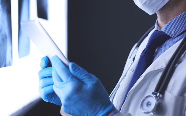 Médecin à l'hôpital assis au bureau regardant des rayons X sur une tablette sur fond blanc avec des rayons X