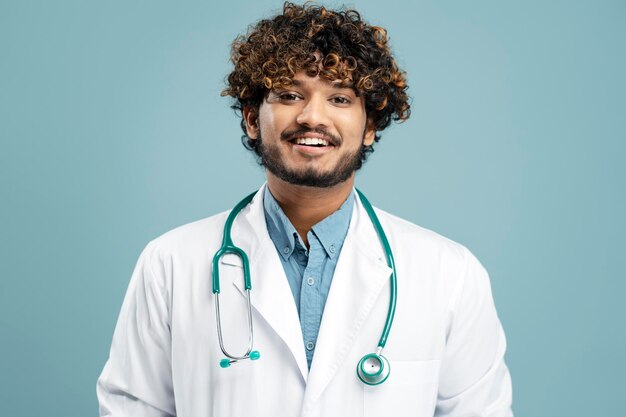 Médecin indien souriant avec stéthoscope portant une blouse de laboratoire isolé sur fond bleu à l'hôpital