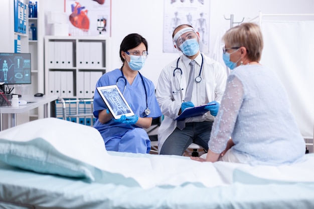 Médecin et infirmière consultant un patient âgé lors d'une épidémie de coronavirus dans une chambre d'hôpital portant un masque facial