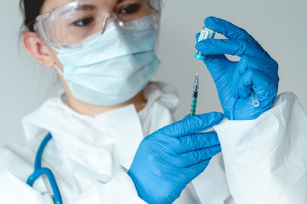 Un médecin ou une infirmière en tenue de protection tient une seringue et un vaccin contre le covid 19