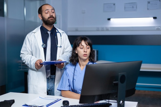 Photo médecin et infirmière travaillant avec la technologie sur ordinateur pour les soins et traitements médicaux. équipe de travailleurs utilisant des fichiers de surveillance et de contrôle pour le système de santé, travaillant tard dans la nuit.