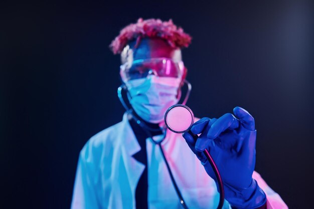 Médecin Intelligent En Uniforme De Protection Tenant Un Stéthoscope éclairage Au Néon Futuriste Jeune Homme Afro-américain Dans Le Studio