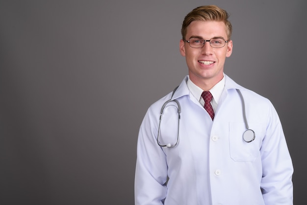 Médecin de jeune bel homme aux cheveux blonds sur mur gris