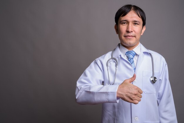 Médecin de jeune homme asiatique contre mur gris