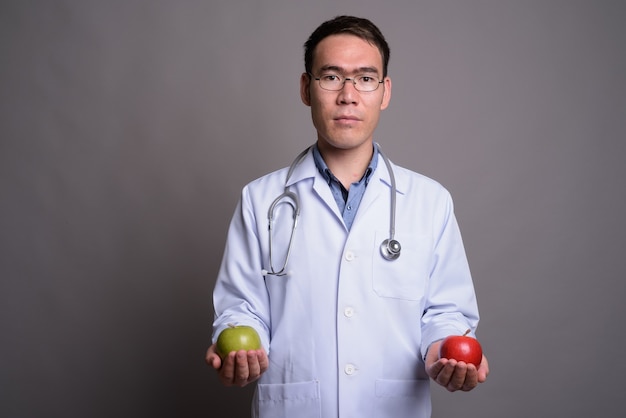 Médecin de jeune homme asiatique contre mur gris