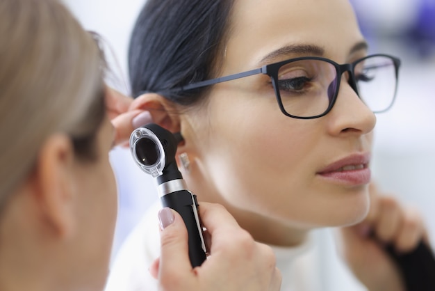 Médecin laryngologiste examinant l'oreille d'une patiente avec des lunettes à l'aide d'un otoscope