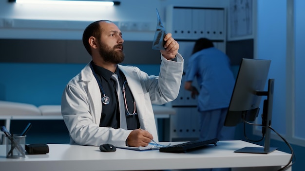 Médecin médecin analysant la radiographie tapant l'expertise médicale sur ordinateur travaillant pendant des heures dans le bureau de l'hôpital. Medic planifiant un traitement médicamenteux pour aider le patient à guérir la maladie. Service de soins de santé