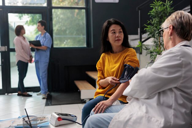 Médecin médecin mesurant l'hypertension et la pression artérielle pour faire un examen cardiaque avec tonomètre dans la zone d'attente de l'hôpital. Médecin consultant un patient asiatique avec instrument de cardiologie, concept de médecine