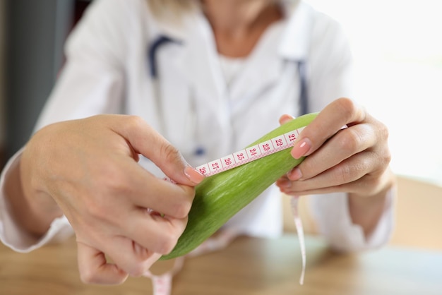 Le médecin mesure la longueur du concombre avec un ruban à mesurer assis à table dans une clinique médicale