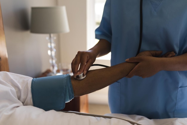 Une médecin mesure la pression artérielle d'un homme âgé dans la chambre à coucher à la maison.
