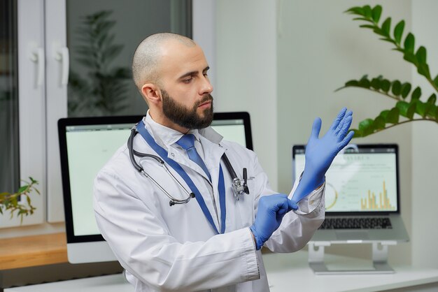 Un médecin met des gants jetables dans son bureau.