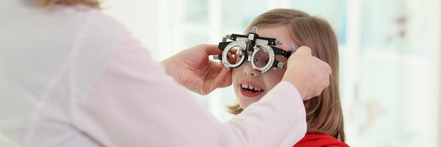 Le médecin met des lunettes d'ophtalmologie sur la petite fille pour vérifier que le spécialiste de la vue effectue un examen