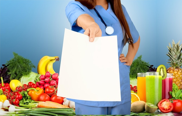 Photo médecin montrant du papier vierge contre des tas de fruits et légumes