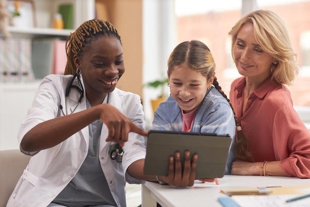 Une médecin montrant une tablette qui consulte une famille dans une clinique pour enfants