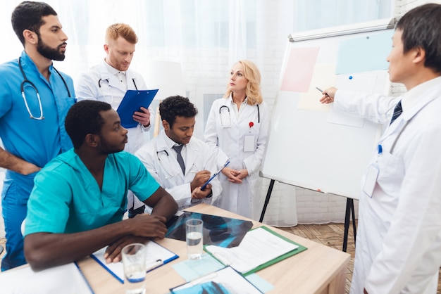 Un médecin montre à d’autres médecins du papier sur un tableau blanc.