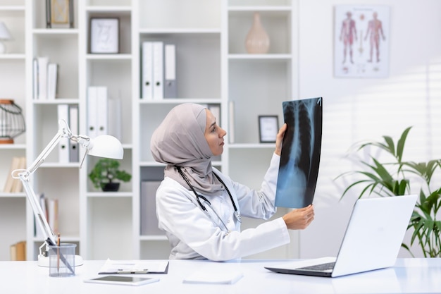 Une médecin musulmane concentrée avec un stéthoscope vérifie les radiographies des poumons alors qu'elle est assise à l'hôpital