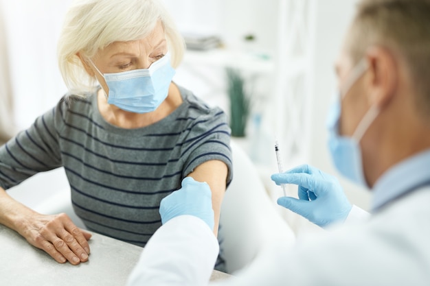 Médecin nettoyant le bras du patient avec un tampon imbibé d'alcool avant l'injection