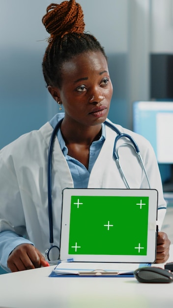 Médecin noir montrant une tablette avec écran vert horizontal au patient lors de la consultation. Médecin afro-américain et femme regardant la clé chroma avec un modèle de maquette isolé à l'écran.