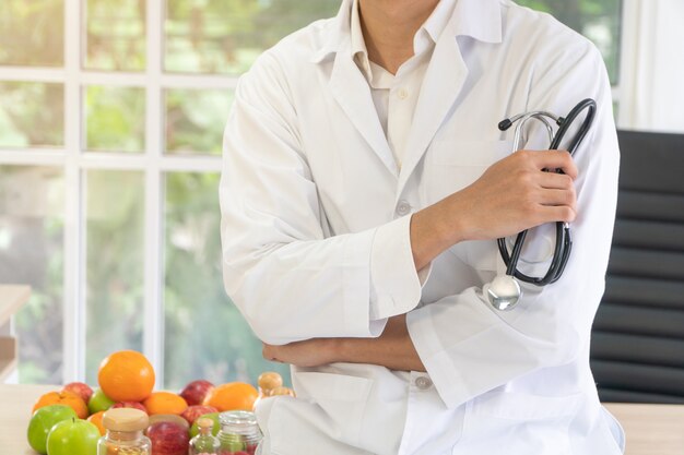 Médecin ou nutritionniste assis sur le bureau avec une bouteille de fruits et de vitamines en clinique.