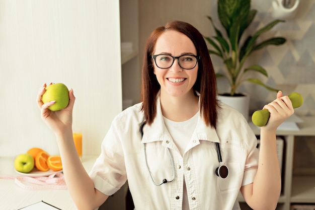Médecin nutritionniste femme dans des verres au travail avec une pomme, kettlebell à la main