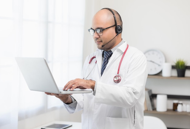 Le médecin parle au patient par vidéoconférence en ligne avec un ordinateur portable portant un casque Expliquer la prise de médicaments pour traiter les maladies