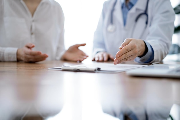 Médecin et patient assis l'un près de l'autre au bureau en bois de la clinique. Femme médecin pointant vers un formulaire d'enregistrement. Notion de médecine