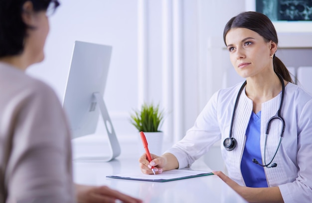 Médecin et patient discutant de problèmes médicaux dans une salle de consultation d'hôpital Doc remplissant le formulaire d'un patient