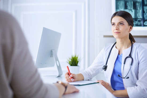 Médecin et patient discutant de problèmes médicaux dans une salle de consultation d'hôpital Doc remplissant le formulaire d'un patient