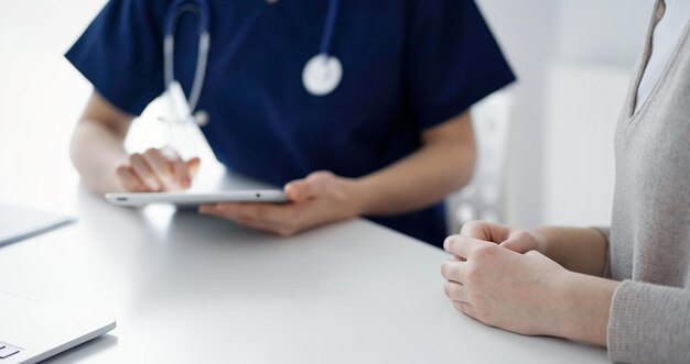 Médecin et patient se parlant en clinique tout en étant assis et en utilisant une tablette, en gros plan. Notion de médecine.