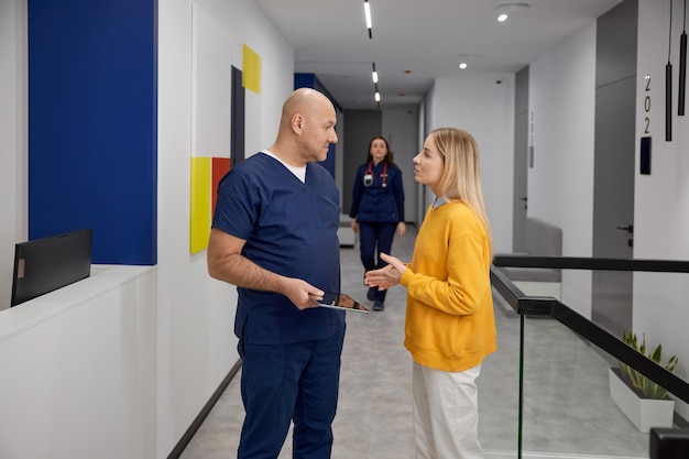 Photo un médecin et une patiente discutent de quelque chose alors qu'ils se tiennent dans le couloir de la clinique.