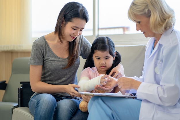 Médecin pédiatre examinant une petite fille asiatique avec un bras cassé portant un plâtre à l'hôpital