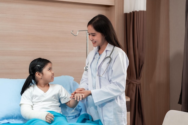 Photo médecin pédiatre examinant une petite fille asiatique avec un bras cassé portant un plâtre à l'hôpital