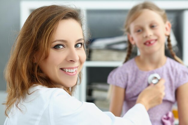 Un médecin pédiatre souriant écoute la respiration et le rythme cardiaque d'une fille avec un stéthoscope