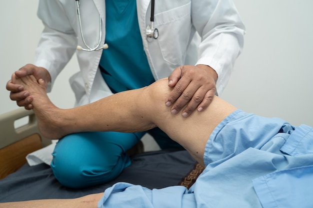 Médecin physiothérapeute asiatique examinant le massage et le traitement du genou et de la jambe d'un patient âgé à l'hôpital d'infirmières de la clinique médicale orthopédiste