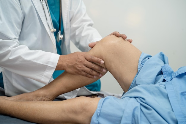 Médecin physiothérapeute asiatique examinant le massage et le traitement du genou et de la jambe d'un patient âgé à l'hôpital d'infirmières de la clinique médicale orthopédiste