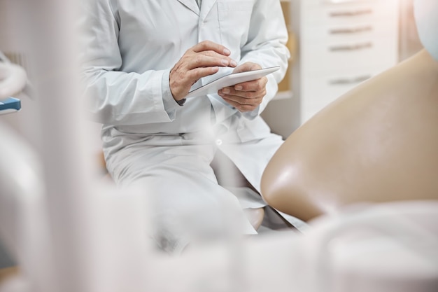 un médecin portant une blouse de laboratoire et tapant sur une tablette alors qu'il était assis au bureau