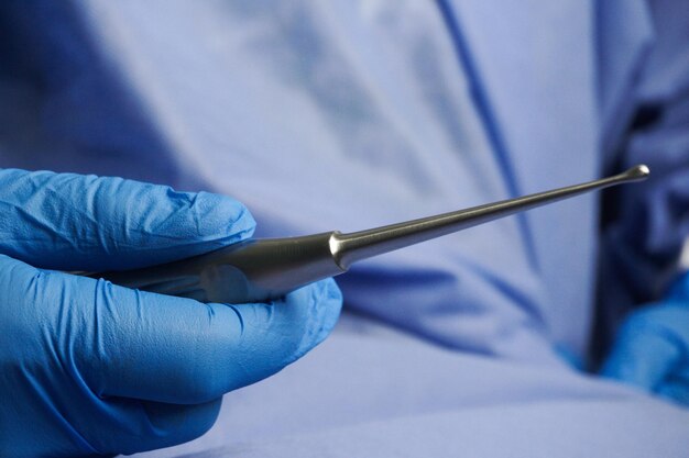 Photo médecin portant des gants médicaux bleus tenant une curette osseuse