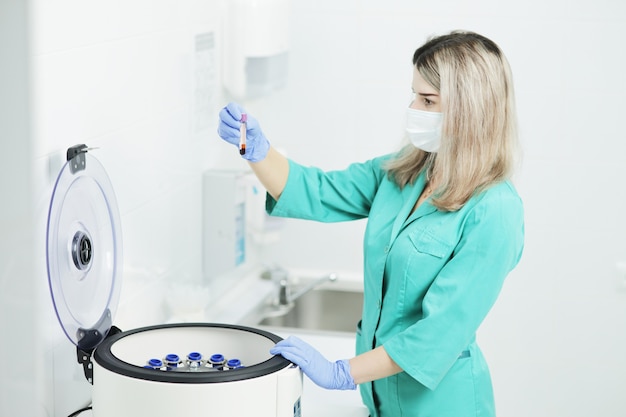 Médecin portant un masque médical est titulaire d'un tube à essai sanguin près d'une centrifugeuse de laboratoire