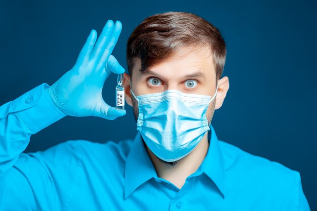 Un médecin portant un masque médical et des gants, vêtu d'un uniforme bleu tient le vaccin contre le coronavirus près de son œil