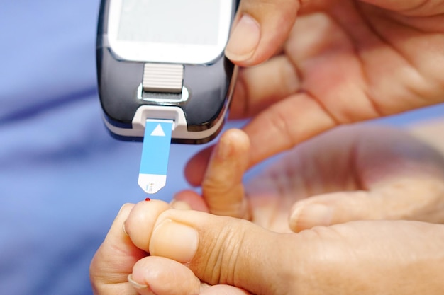 Le médecin porte des gants à l'aide d'une lancette sur le doigt pour vérifier le niveau de sucre dans le sang par un lecteur de glycémie