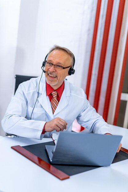 Médecin positif ayant une consultation en ligne au bureau de la clinique avec un ordinateur portable Consultation à distance pandémie blanche