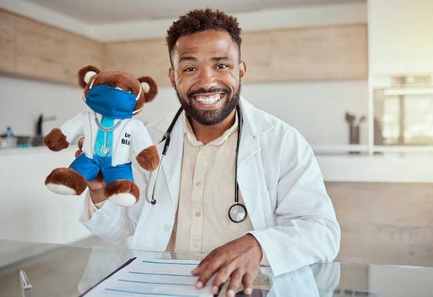 Médecin pour enfants pédiatre et travail de soins de santé tenant un jouet d'ours en peluche et ayant l'air heureux et amical assis dans son bureau dans un hôpital Soins de santé et sourire d'un médecin de sexe masculin